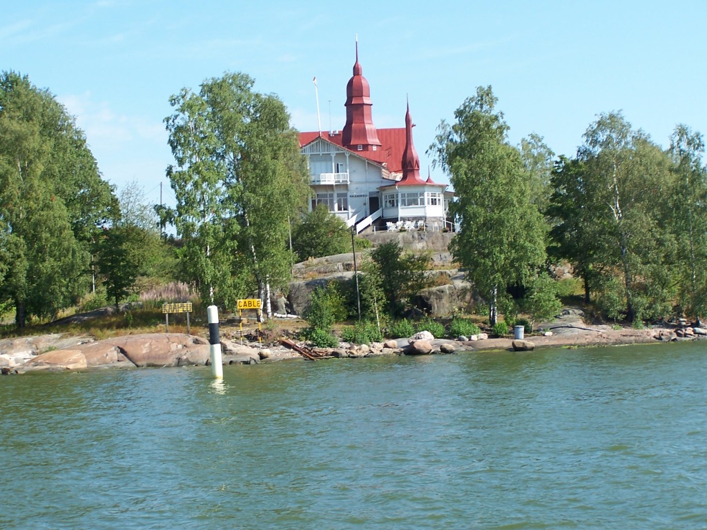 granite island with white building with pointy red roofs and onion shaped turrets.  Trees partly hide the restaurant and cover the rest of the island.  