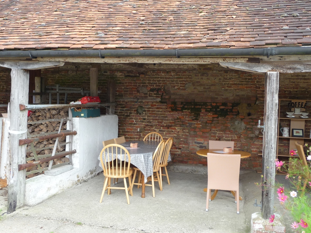 chairs and tables set out under shelter of old farm building.